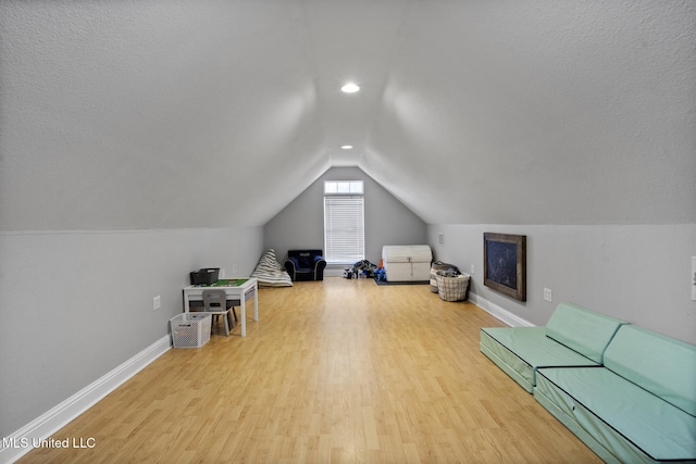 interior space with a textured ceiling, lofted ceiling, baseboards, and wood finished floors