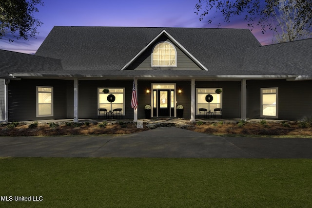 view of front of property featuring covered porch, a shingled roof, and a yard