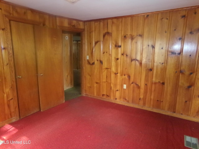 unfurnished bedroom with visible vents, wood walls, and carpet