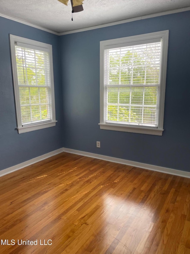 empty room with a wealth of natural light, crown molding, a textured ceiling, and hardwood / wood-style floors