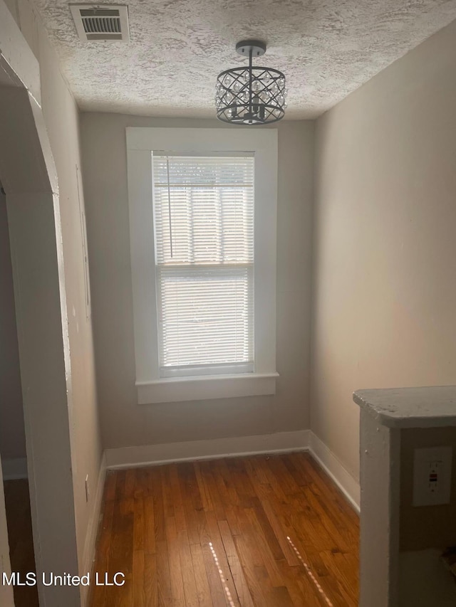 unfurnished dining area featuring a textured ceiling and dark hardwood / wood-style flooring