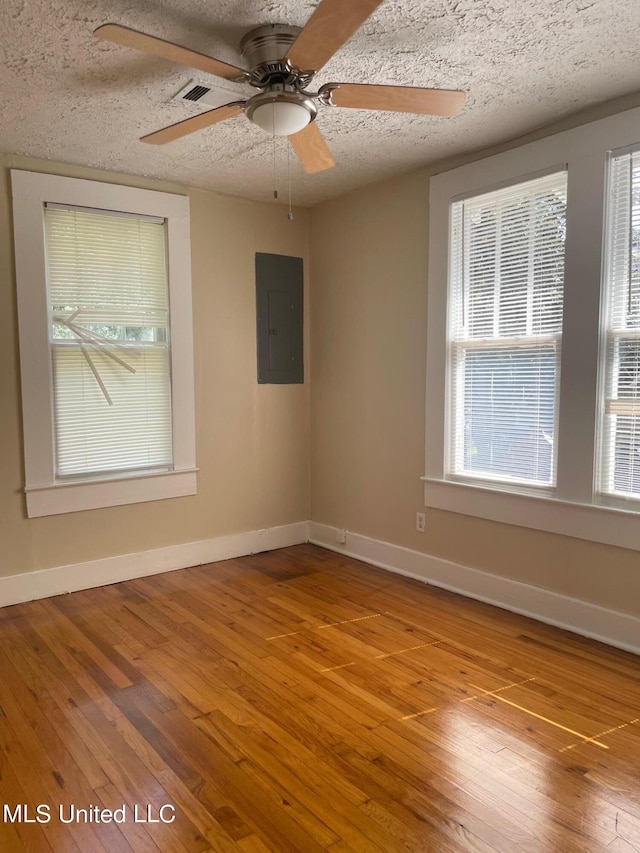 spare room featuring a textured ceiling, electric panel, and light hardwood / wood-style flooring