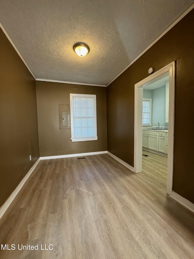 empty room with a textured ceiling, sink, electric panel, light hardwood / wood-style flooring, and crown molding