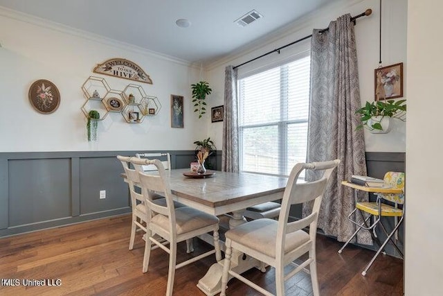 dining room featuring visible vents, crown molding, a wainscoted wall, wood finished floors, and a decorative wall