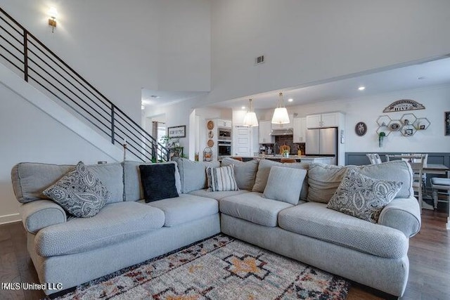 living area with visible vents, stairway, a towering ceiling, and dark wood-style flooring