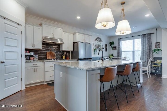 kitchen featuring white cabinetry, under cabinet range hood, freestanding refrigerator, and ornamental molding