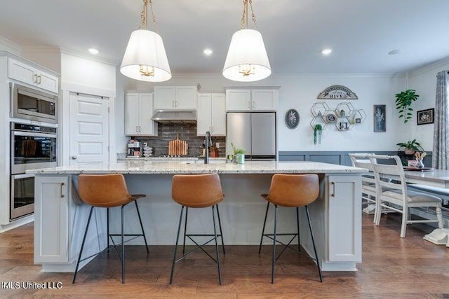 kitchen featuring backsplash, under cabinet range hood, ornamental molding, appliances with stainless steel finishes, and a large island