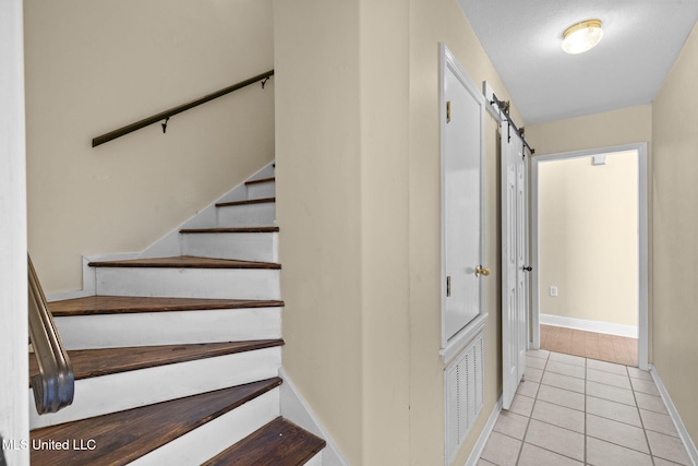 staircase featuring baseboards, a barn door, visible vents, and tile patterned floors