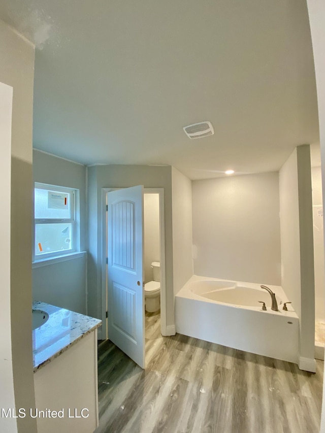 bathroom with a washtub, vanity, hardwood / wood-style flooring, and toilet