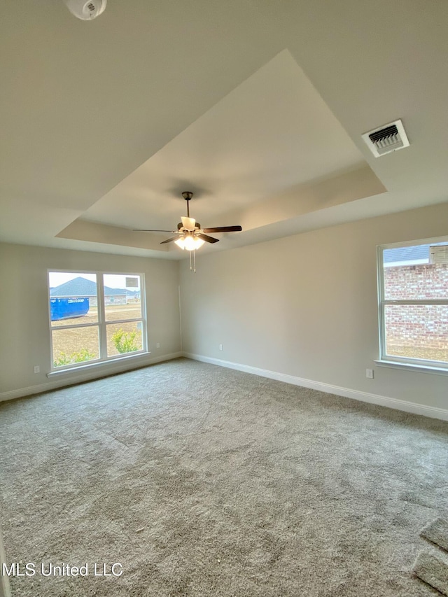 carpeted spare room with a tray ceiling and ceiling fan