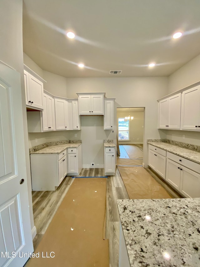 kitchen with light stone counters, light hardwood / wood-style flooring, and white cabinets