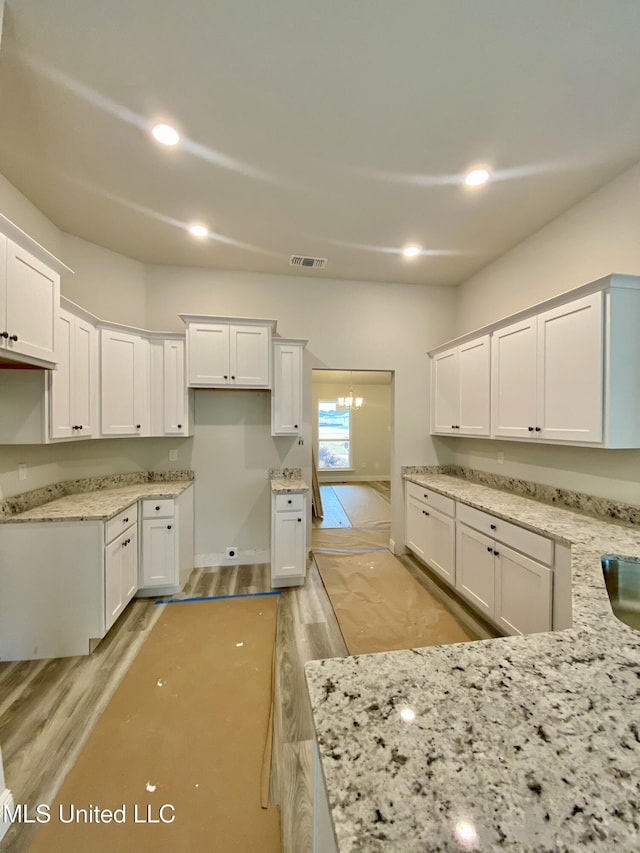 kitchen with light stone countertops, light wood-type flooring, white cabinetry, and sink