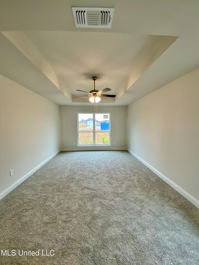 spare room with a tray ceiling, ceiling fan, and carpet