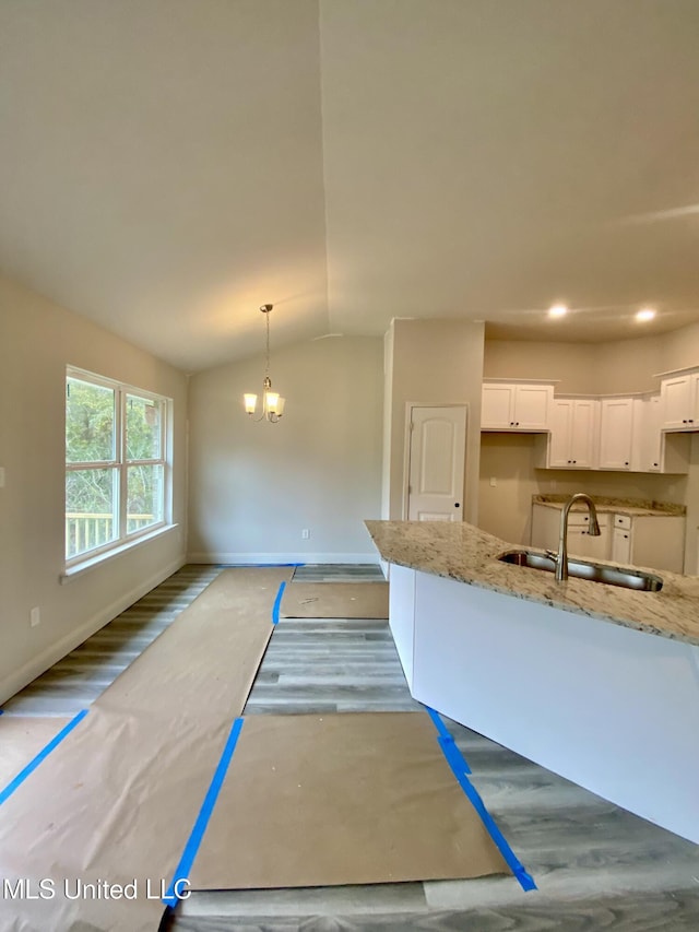 kitchen with vaulted ceiling, white cabinetry, hanging light fixtures, and light stone counters