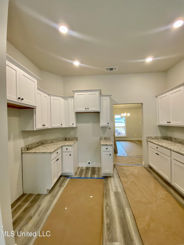 kitchen with white cabinetry, light hardwood / wood-style floors, light stone counters, and a notable chandelier