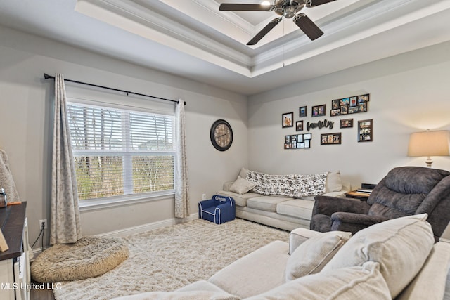 living area featuring ornamental molding, a ceiling fan, a tray ceiling, carpet floors, and baseboards