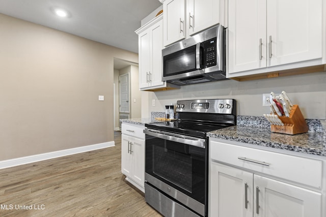 kitchen with light wood finished floors, appliances with stainless steel finishes, stone countertops, and baseboards