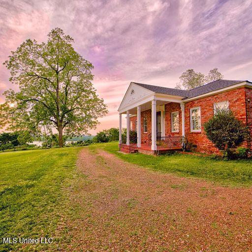 property exterior at dusk featuring a porch and a lawn