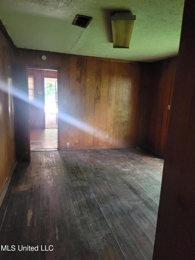 unfurnished room with wooden walls, a textured ceiling, and dark hardwood / wood-style flooring