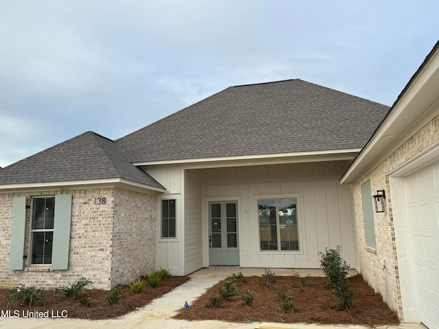 property entrance with brick siding, roof with shingles, and an attached garage