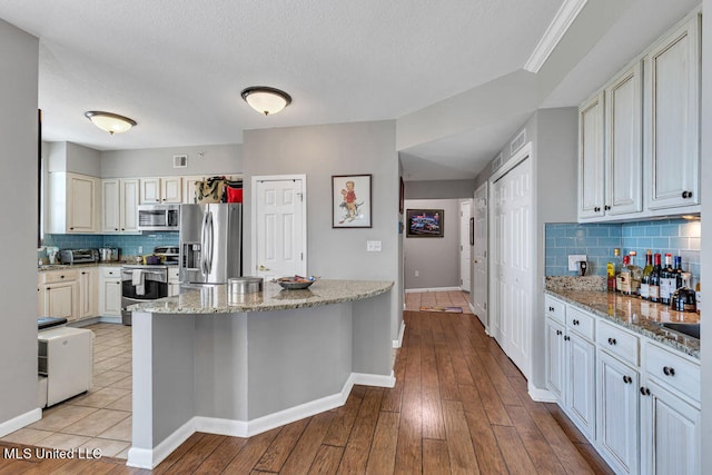 kitchen featuring stainless steel appliances, light wood-type flooring, light stone counters, a textured ceiling, and tasteful backsplash