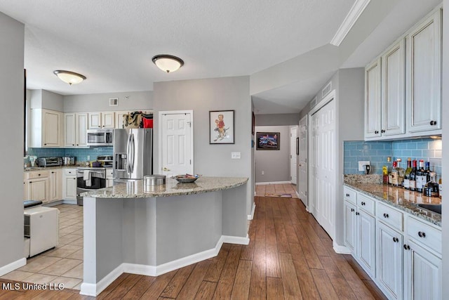 kitchen with a kitchen island, baseboards, light wood-style floors, appliances with stainless steel finishes, and backsplash