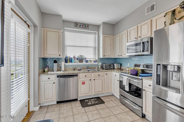kitchen with backsplash, visible vents, light stone countertops, a sink, and stainless steel appliances