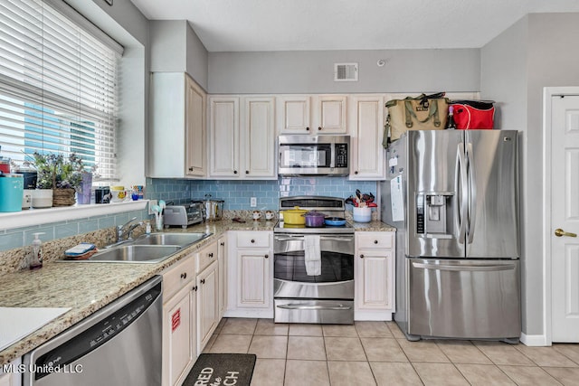 kitchen featuring tasteful backsplash, appliances with stainless steel finishes, sink, light stone counters, and light tile patterned floors