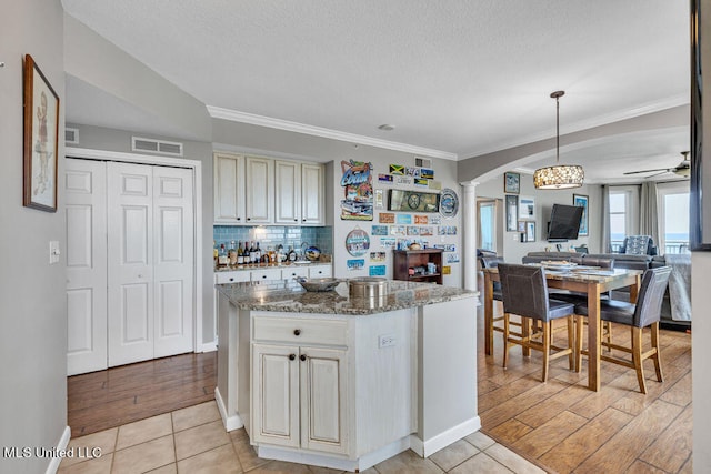 kitchen featuring cream cabinets, light wood-type flooring, stone countertops, ornate columns, and decorative light fixtures