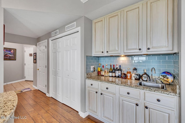 kitchen featuring light stone counters, sink, light wood-type flooring, and backsplash