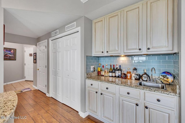 kitchen featuring visible vents, a sink, baseboards, and tasteful backsplash