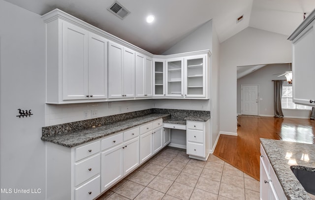 603 Charmant Pl, Ridgeland, MS 39157 - kitchen with lofted ceiling, white cabinets, glass insert cabinets, light tile patterned floors, and dark stone countertops