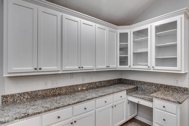 603 Charmant Pl, Ridgeland, MS 39157 - kitchen with lofted ceiling, white cabinets, glass insert cabinets, light stone countertops, and decorative backsplash