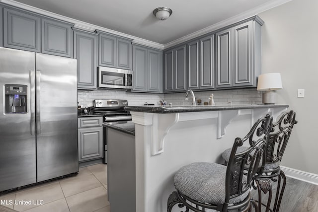 kitchen with gray cabinets, a breakfast bar, backsplash, stainless steel appliances, and kitchen peninsula