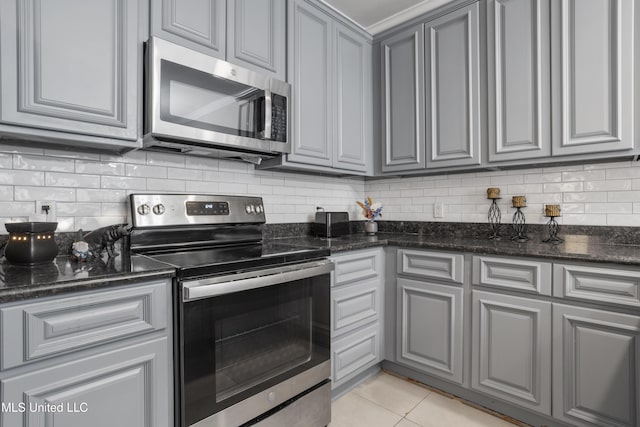 kitchen featuring light tile patterned floors, decorative backsplash, dark stone counters, and appliances with stainless steel finishes