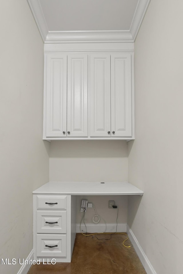 unfurnished office featuring built in desk, ornamental molding, baseboards, and concrete floors