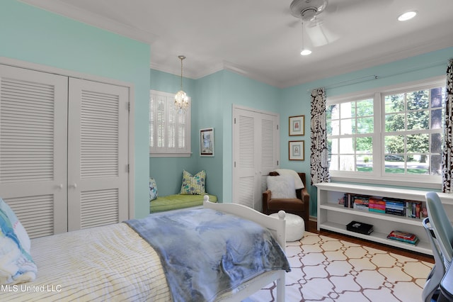 bedroom featuring ornamental molding, ceiling fan with notable chandelier, and two closets