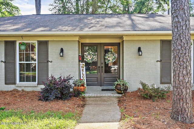 doorway to property featuring brick siding, french doors, and a shingled roof