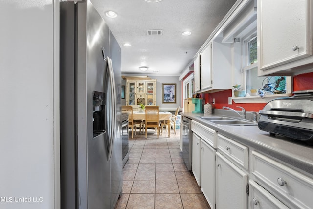 kitchen featuring appliances with stainless steel finishes, light tile patterned flooring, sink, a textured ceiling, and white cabinets