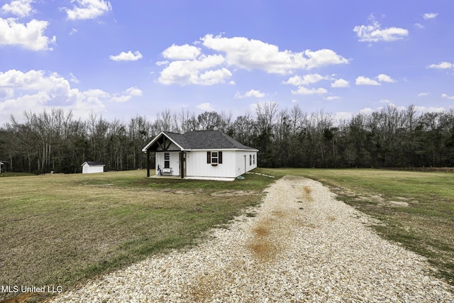 view of front facade with a storage unit, a wooded view, an outdoor structure, driveway, and a front lawn