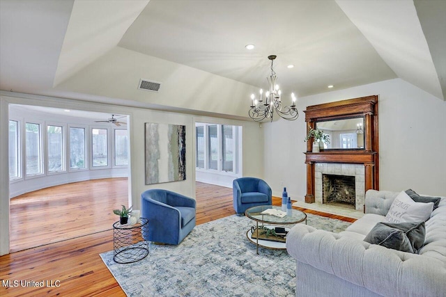 living room with hardwood / wood-style floors, a tiled fireplace, ceiling fan with notable chandelier, and plenty of natural light