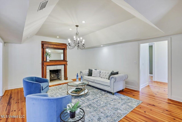 living room with an inviting chandelier, wood-type flooring, a fireplace, and lofted ceiling