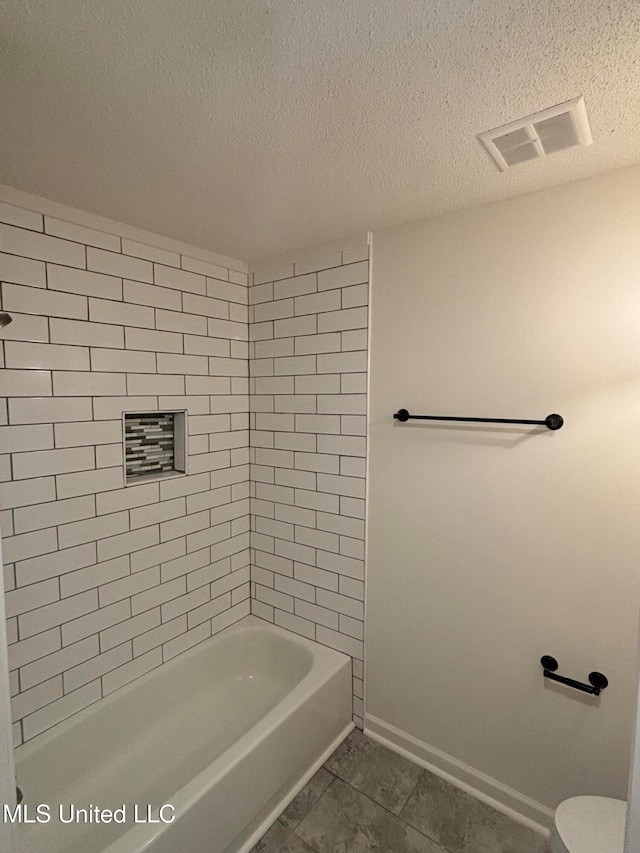 bathroom featuring tiled shower / bath, a textured ceiling, toilet, and tile patterned flooring