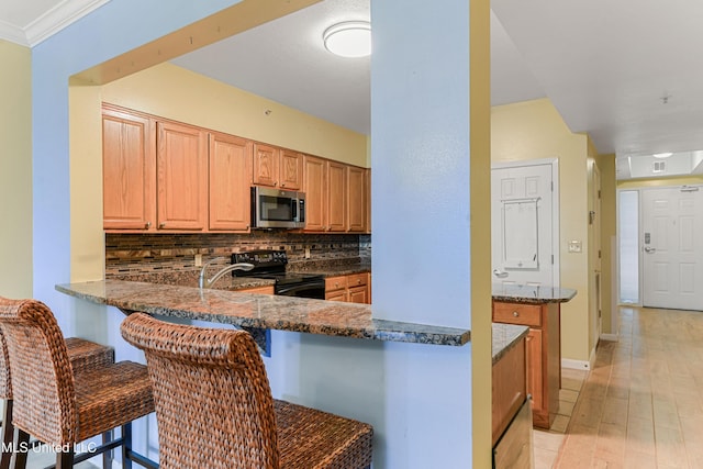 2230 Beach Dr Unit 205, Gulfport, MS 39507 - kitchen with black range with electric stovetop, stainless steel microwave, tasteful backsplash, a kitchen bar, and dark stone countertops