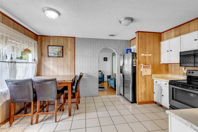 5608 Claresholm Dr, Gautier, MS 39553 - kitchen with stainless steel appliances, arched walkways, wooden walls, white cabinetry, and a textured ceiling