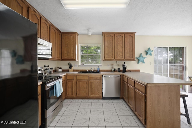kitchen featuring stainless steel appliances, a peninsula, light marble finish flooring, a sink, and a textured ceiling