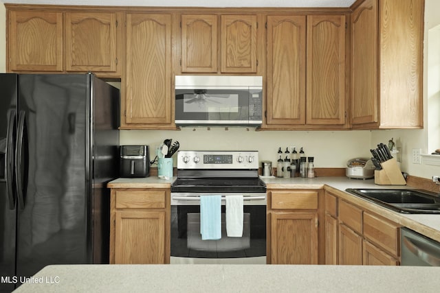 kitchen with stainless steel appliances, light countertops, a sink, ceiling fan, and brown cabinetry