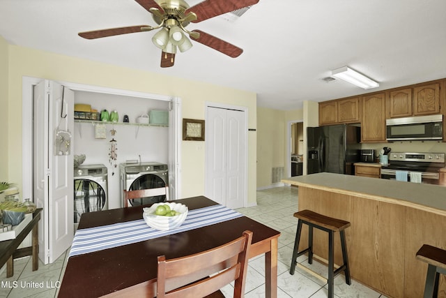 kitchen with stainless steel appliances, separate washer and dryer, a ceiling fan, a breakfast bar, and brown cabinets