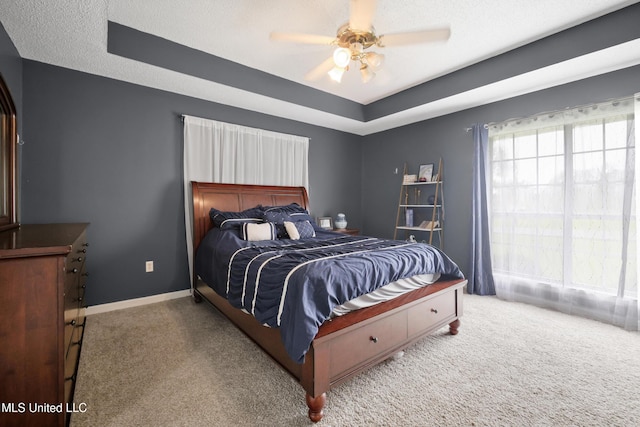bedroom featuring carpet, a tray ceiling, ceiling fan, and baseboards