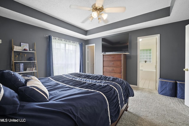 bedroom featuring carpet floors, a tray ceiling, ensuite bathroom, ceiling fan, and a textured ceiling